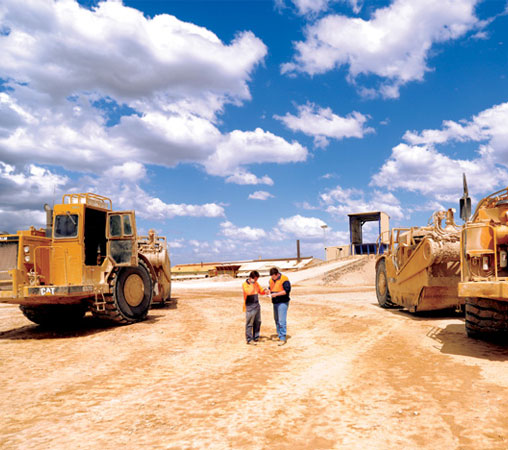 A photo of two workmen standing infront of earth moving equipment
